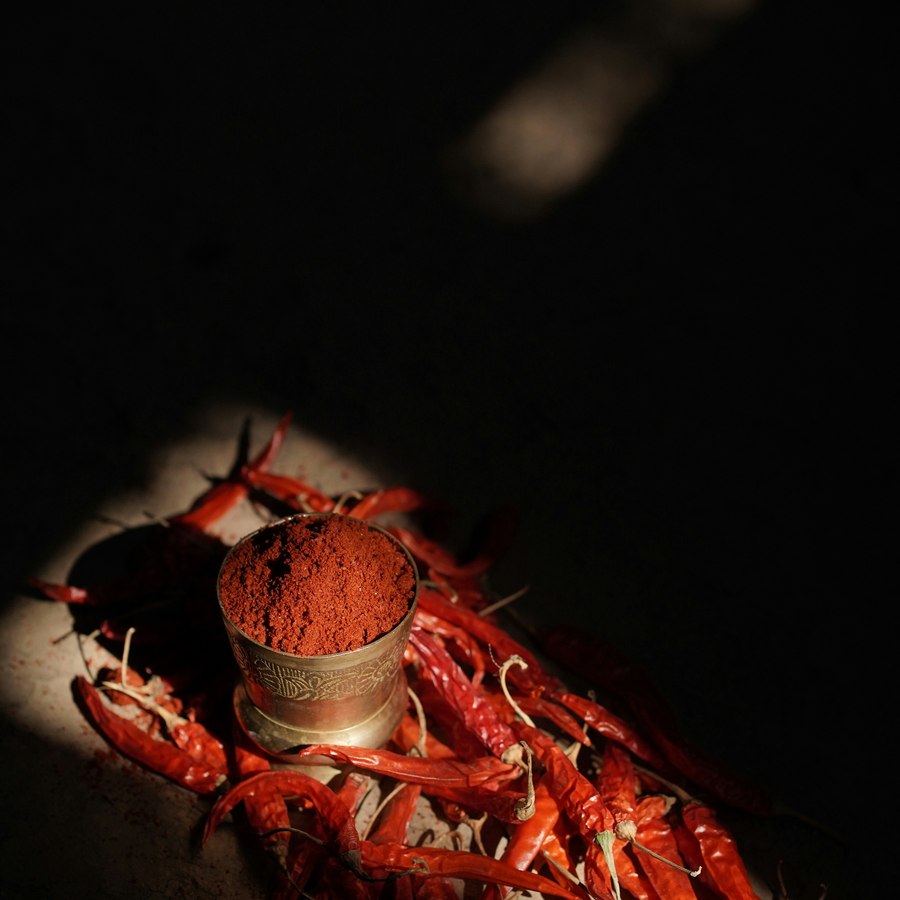 Red chilli powder in a metal cup surrounded by dried red chillies